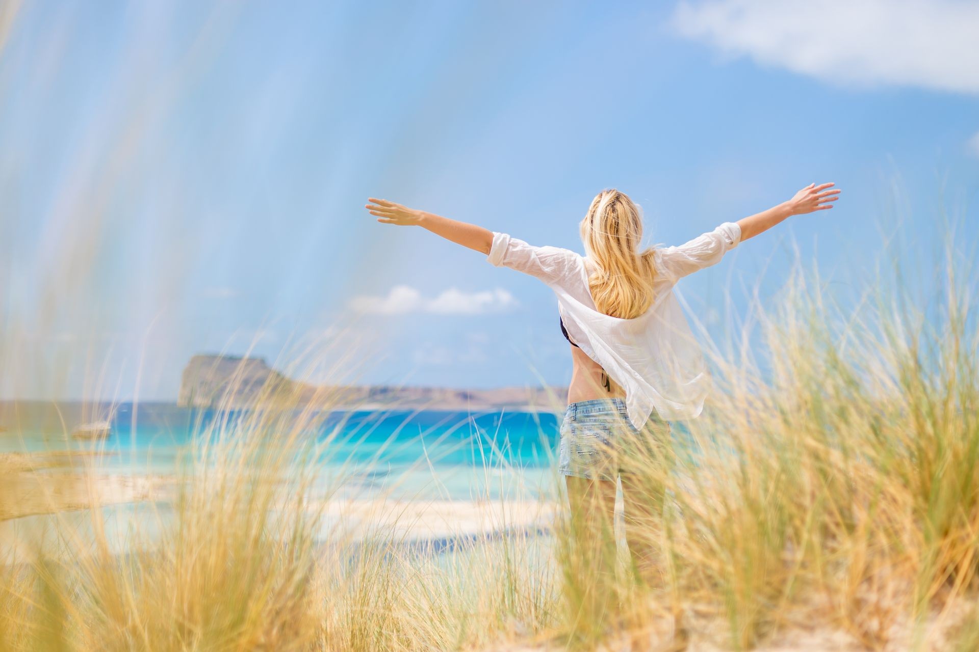 Relaxed woman, arms rised, enjoying sun, freedom and life an a beautiful beach. Young lady feeling free, relaxed and happy. Concept of vacations, freedom, happiness, enjoyment and well being.